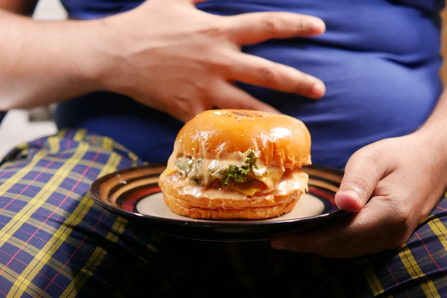 man holding his stomach with a burger in front of him