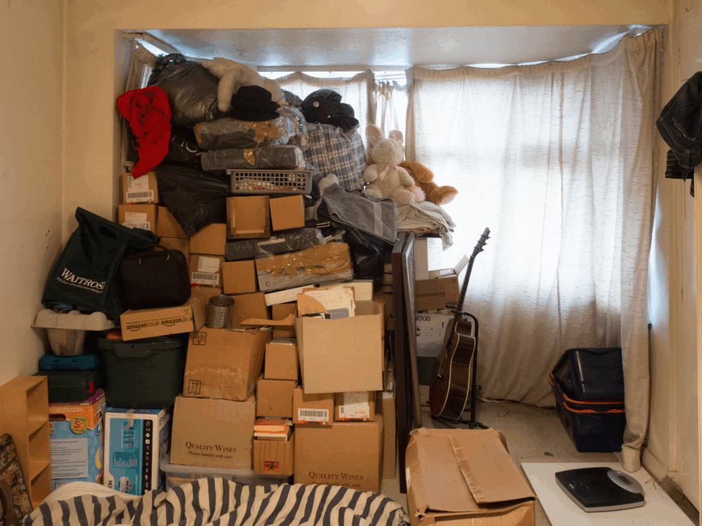 Room completely filled floor to ceiling with boxes, clothes, and belongings stacked against window, demonstrating how decision paralysis leads to overwhelming accumulation.