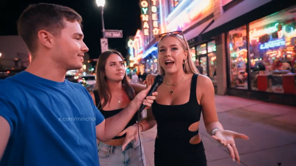 The woman gestures naturally while speaking into the microphone during what appears to be an authentic street interview. The synthetic footage showcases perfectly synced facial expressions, natural hand movements, and convincing urban lighting that would fool anyone into thinking they're watching real people having a real conversation.