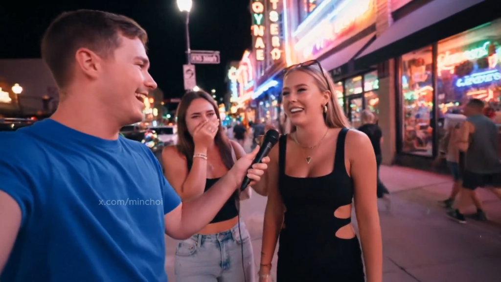 Image 1: A young man in a blue t-shirt holds a microphone toward a blonde woman in a black sleeveless top with cutout details while a third person stands between them on a bustling nighttime street lined with neon signs and storefronts. This entire scene was generated by Google DeepMind's Veo 3 from a simple text prompt. No cameras, no crew, no actual people.