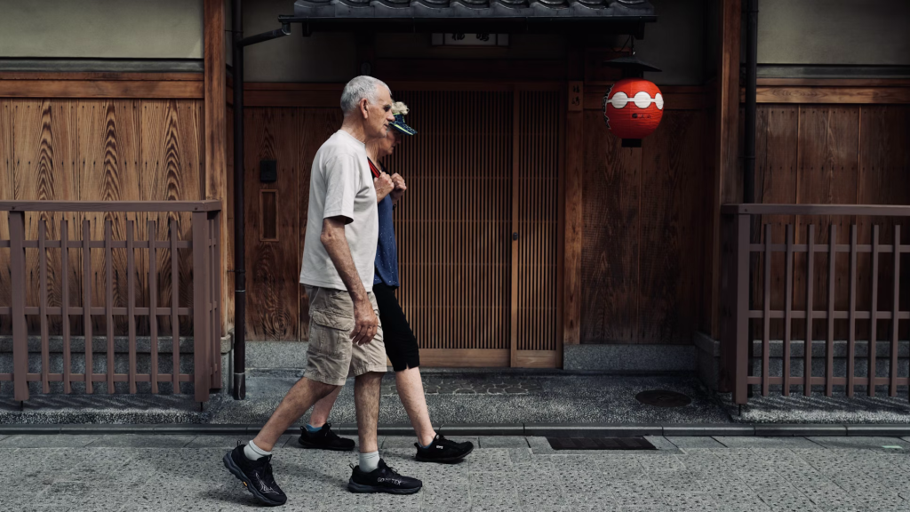 Two people walking past traditional Japanese architecture with wooden lattice doors and a red lantern.