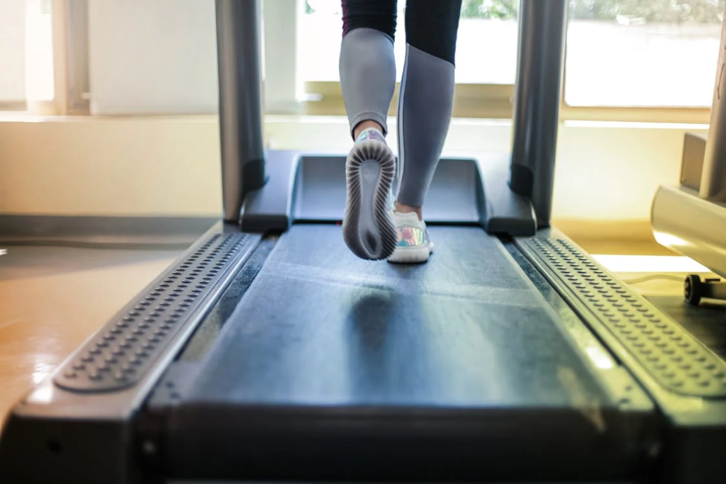 Close-up of legs in black leggings and athletic shoes walking on a treadmill belt.