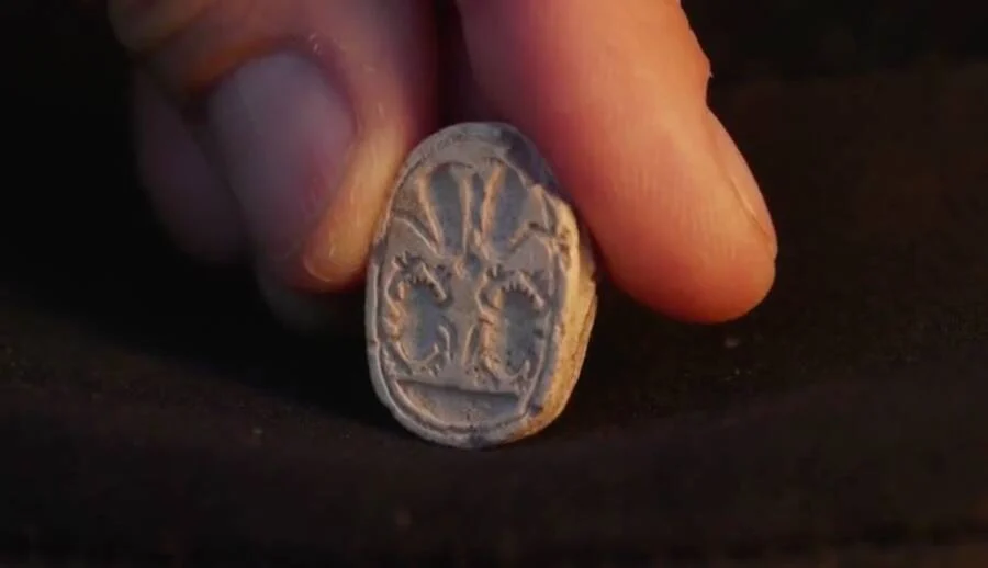Fingers holding the stone amulet, depicting the scarabs.