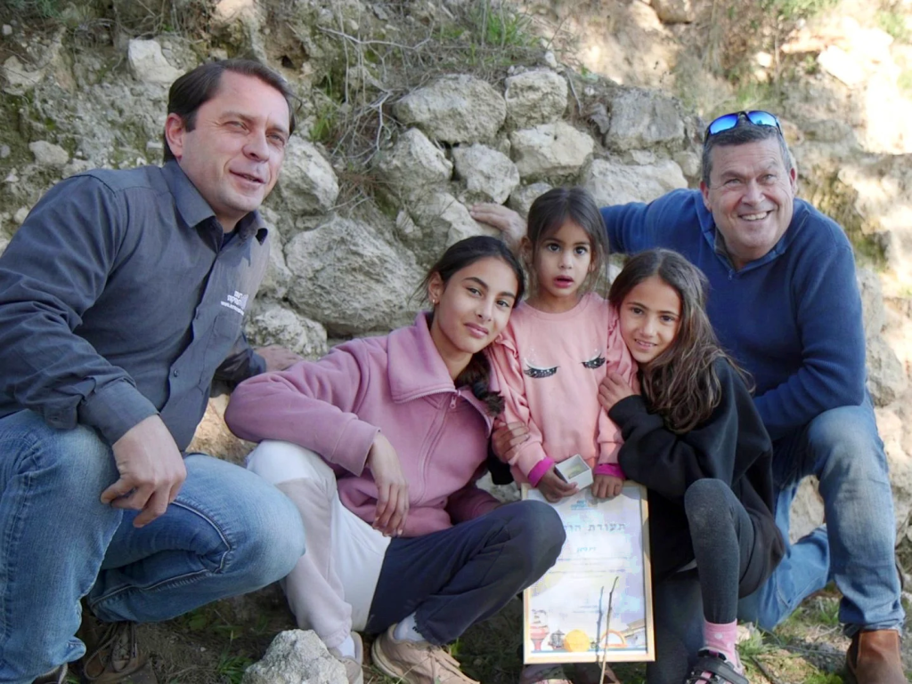 Authority) A three-year-old Israeli girl has found a scarab-shaped Canaanite amulet dating back some 3,800 years at the site of Tel Azeka near Bet Shemesh, the Israel Antiquities Authority (IAA) announced Tuesday. Ziv Nitzan, from Moshav Ramot Meir, was hiking with her parents and two older sisters at the foot of the hill where the archaeological site stands when she picked up what appeared to be a small stone. “We were walking along the path, and then Ziv bent down – and out of all the stones around her, she picked up this particular stone,” Omer Nitzan, Ziv’s sister, said in a statement sent out by the IAA. “When she rubbed it and removed the sand from it, we saw something was different about it. I called my parents to come see the beautiful stone, and we realized we had discovered an archaeological find! We immediately reported this to the Israel Antiquities Authority.” Promoted: Identity/Crisis w/ Tal Becker Keep Watching Scarab amulets trace their origins to ancient Egypt, where beetles were revered as sacred symbols of renewal. Egyptians believed these insects embodied new life, as they laid their eggs inside the dung balls they rolled — seemingly bringing life from decay. “Scarabs were used in this period as seals and as amulets,” Dr. Daphna Ben-Tor, an expert in the field, said in a statement. “They were found in graves, in public buildings, and in private homes. Sometimes they bear symbols and messages that reflect religious beliefs or status.” Get The Times of Israel's Daily Edition by email and never miss our top stories Newsletter email address Your email Get it By signing up, you agree to the terms Ben-Tor examined the artifact found at Tel Azeka and determined its cultural affiliation with the Canaanites, an ancient people recorded throughout the Bible and in historical documents up to 3,500 years old — as well as older archaeological findings — as a group of peoples living throughout the Levant who were ruled by their own city/state kings. From right to left – Tel Aviv University Prof. Oded Lipschits, Noga, Ziv and Omer Nitzan, and Antiquities Authority archaeologist Semyon Gendler