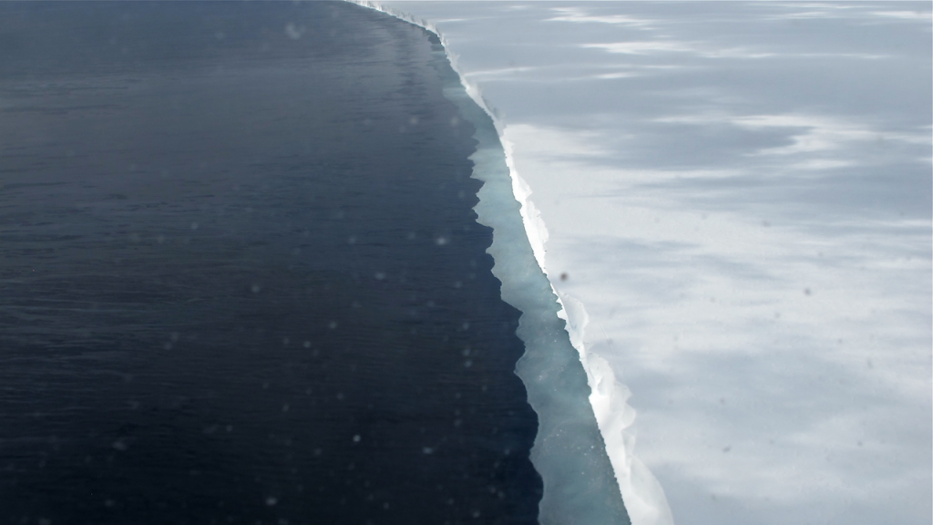 Aerial photograph of a massive Antarctic ice shelf edge meeting dark ocean water.