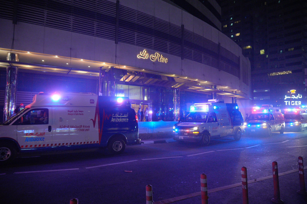 Emergency vehicles with flashing lights respond to a Dubai skyscraper fire at Marina Pinnacle Tower, with multiple ambulances positioned outside the high-rise building.