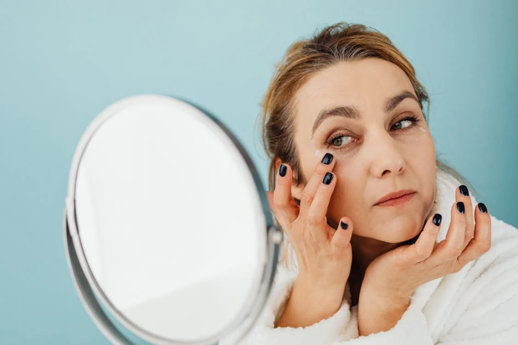 A Woman Looking at the Mirror while Applying a Cream on Her Face
