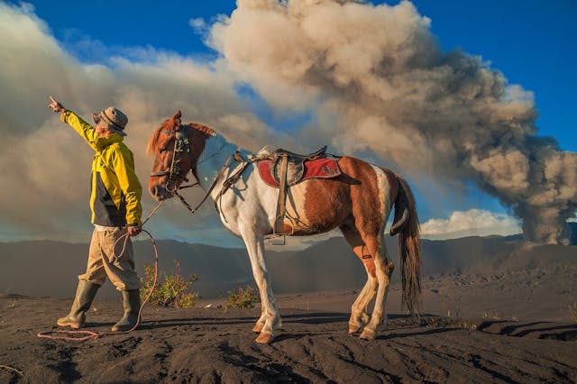man walking with horse, volcanic plume in the background