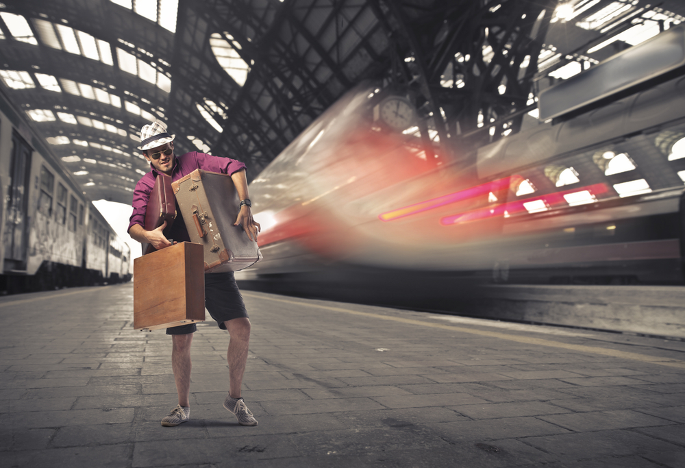 Young tourist carrying many suitcases on the platform of a train station