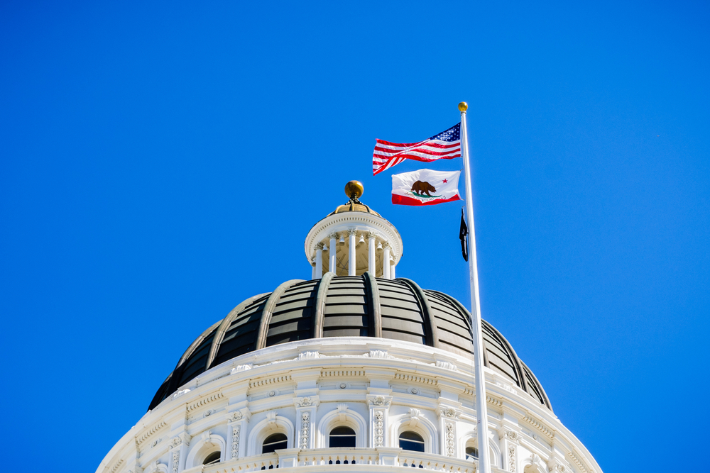 April 14, 2018 Sacramento / CA / USA - The US and the California state flag waving in the wind in front of the dome of the California State Capitol