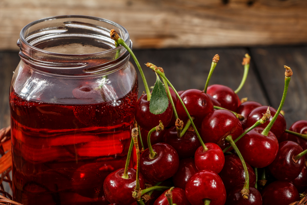 Cherry juice and fresh cherries on a wooden background. Fresh cherry juice in a glass. Fresh cherry on a wooden table.
