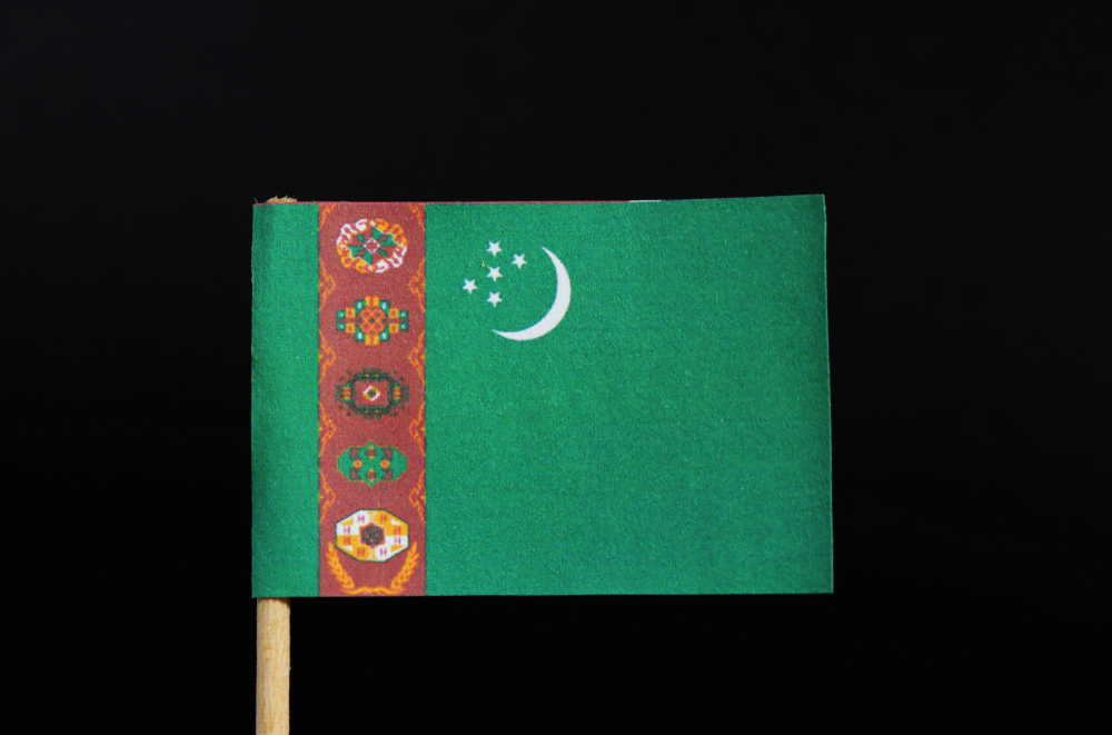 The national flag of Turkmenistan on toothpick on black background. A green field with a vertical red stripe near the hoist side.