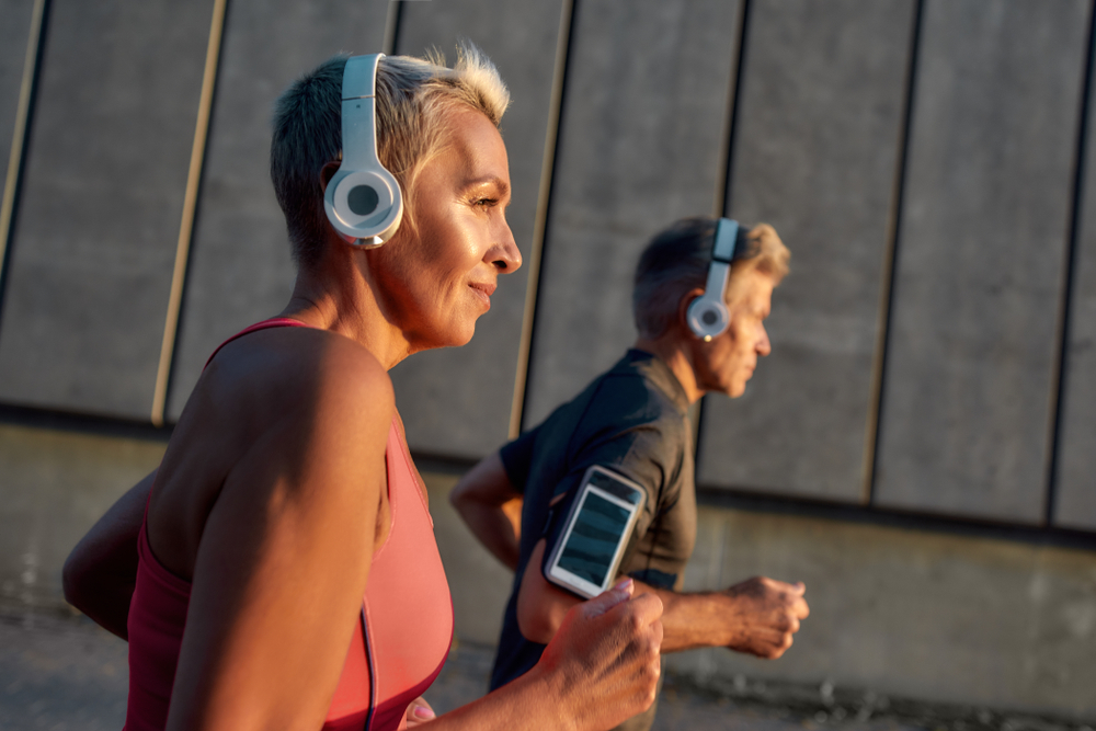 Morning jog. Happy and healthy middle-aged couple in headphones running together through the city street in the morning