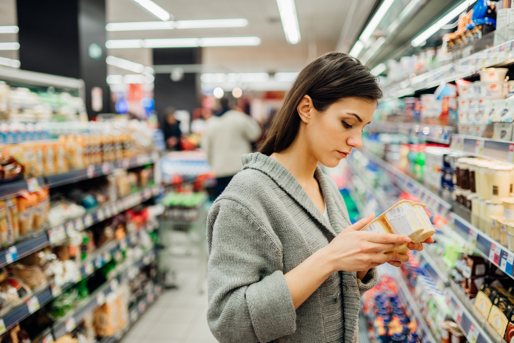 Woman shopping a dairy product in the supermarket grocery store.Reading ingredients,declaration or expiration date before buying it.Nutritional value of the food.Lactose intolerance information