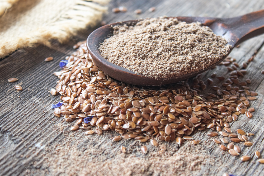 Crushed flax seed in a wooden spoon on a pile of flaxseed. Ground seed is used to prevent heart disease and being overweight.