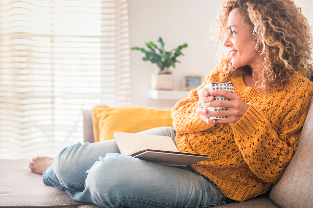 Woman have relax at home with cup of tea and book - reading activity for adult beautiful female people - enjoying quiet lifestyle indoor and long blonde curly hair - happy adult female indoor - people