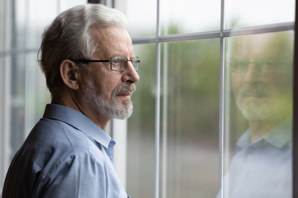 Pensive elderly mature senior man in eyeglasses looking in distance out of window, thinking of personal problems. Lost in thoughts elderly middle aged grandfather suffering from loneliness, copy space
