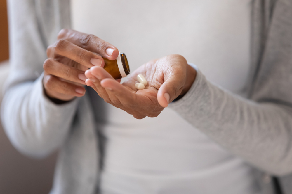 Close up young african ethnicity biracial woman pouring pills from bottle, taking daily dose of complex vitamins or prescribed medicine antibiotics, reducing painful feelings or strengthen immunity.
