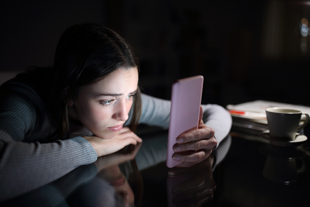 Sad female checking smart phone content in the dark night at home