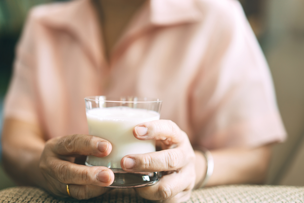 Elderly people health care at home concept. Senior asian woman hand holding a milk glass wear pink shirt in living room.