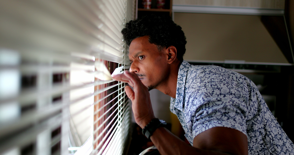 African man looking through window blinds