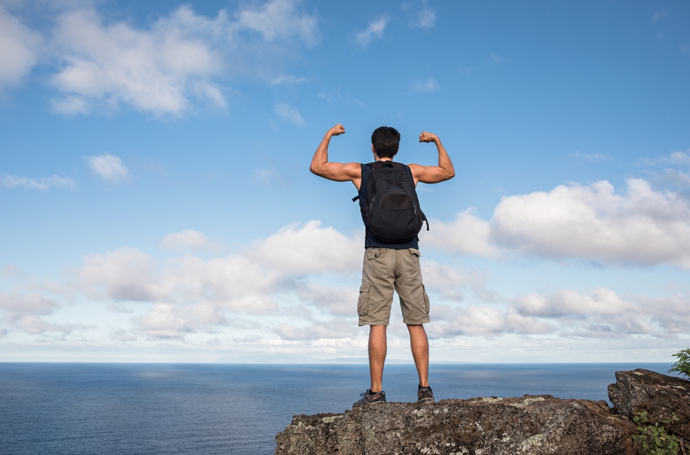 Strong fit man flexing his arms up on a mountain. Mental and physical strength concept.