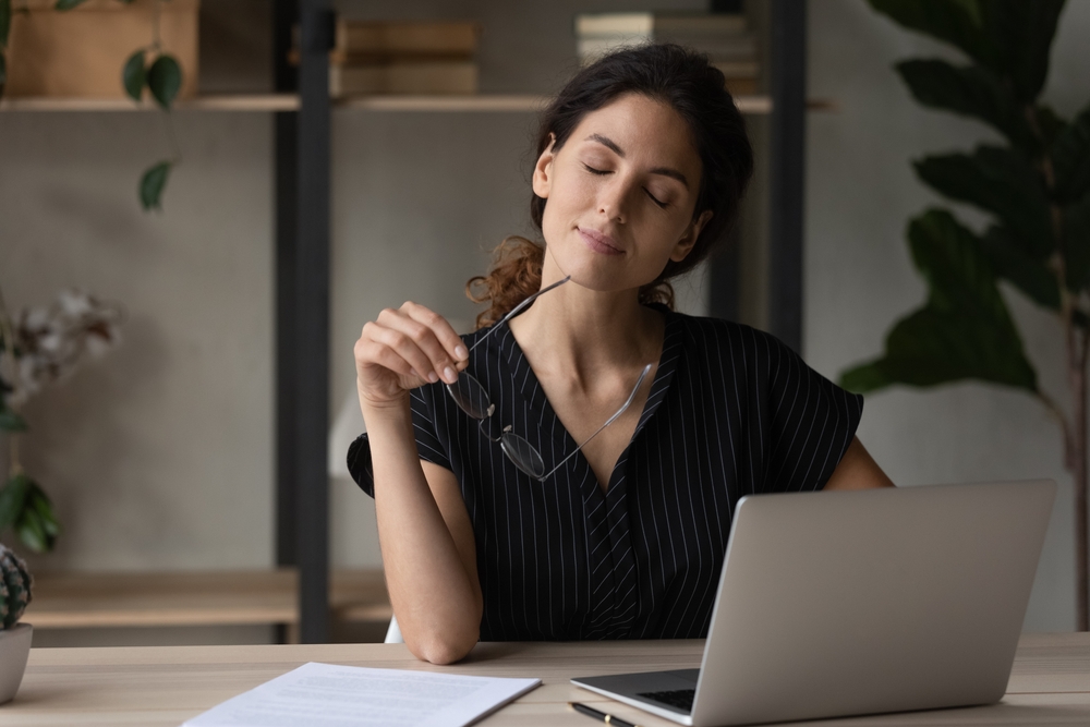 Putting job on pause. Calm latina woman relax at desk take break from computer work hold eyewear in hand give rest to tired eyes. Young lady employee sit on workplace with closed eyes take glasses off
