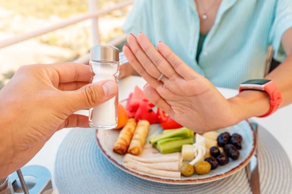 Woman in a restaurant refuses the offered salt and pepper shaker with a gesture of her hand. Diet for gout and high cardiovascular blood pressure