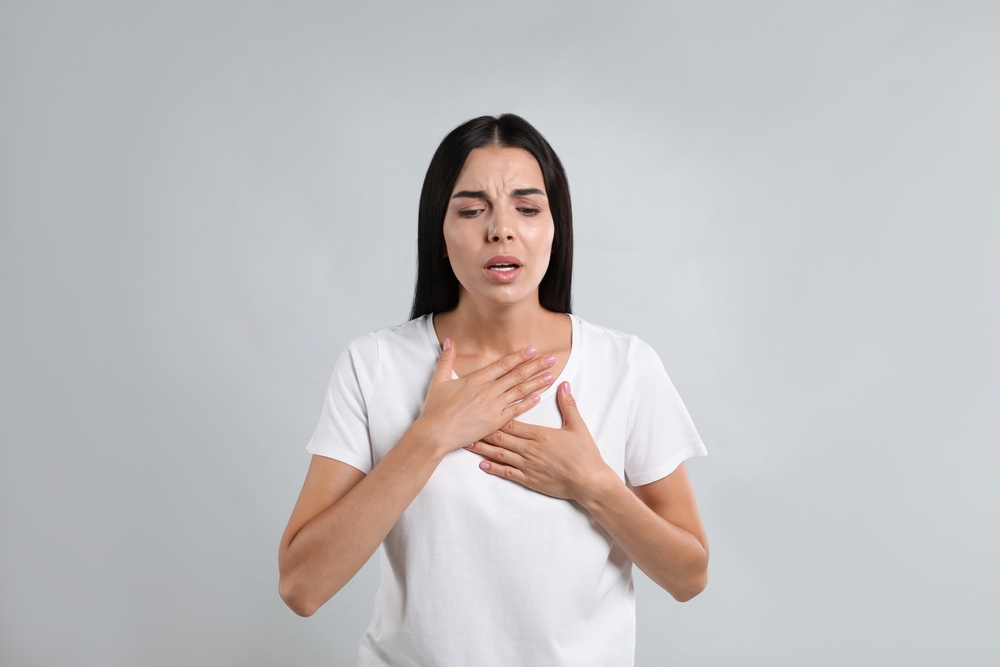 Young woman suffering from breathing problem on light background