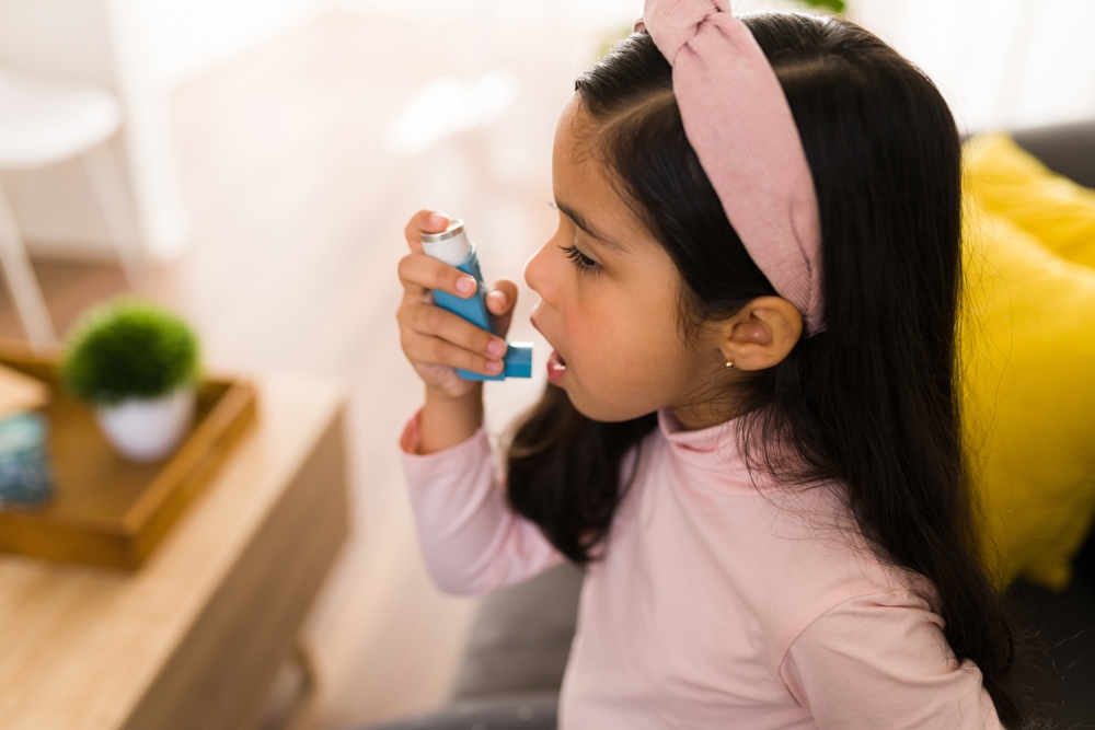 Side view of a cute little girl with breathing problems using an asthma inhaler
