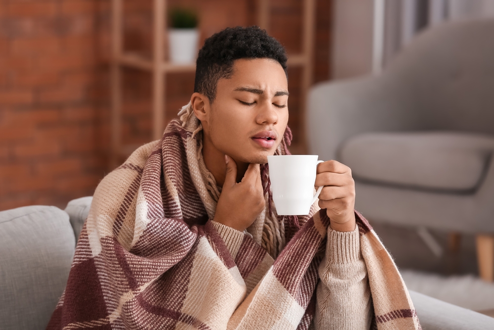 Ill African-American guy with sore throat drinking hot tea at home
