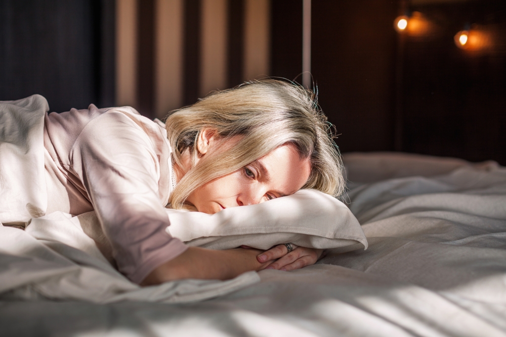Tired middle aged woman lying in bed can't sleep late at morning with insomnia. Adult lady sick or sad depressed sleeping at home.