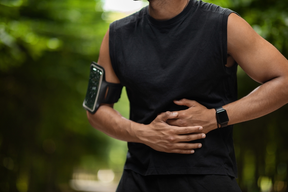 Cropped of african american sportsman exercising in public park, touching left side, experiencing acute pain while having workout outdoors, copy space. Abdominal pain and sports concept