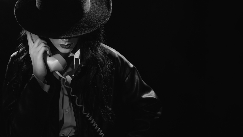 Dark noir portrait of a female detective holding a retro telephone receiver. Private detective, spy, investigation concept. black and white snapshot