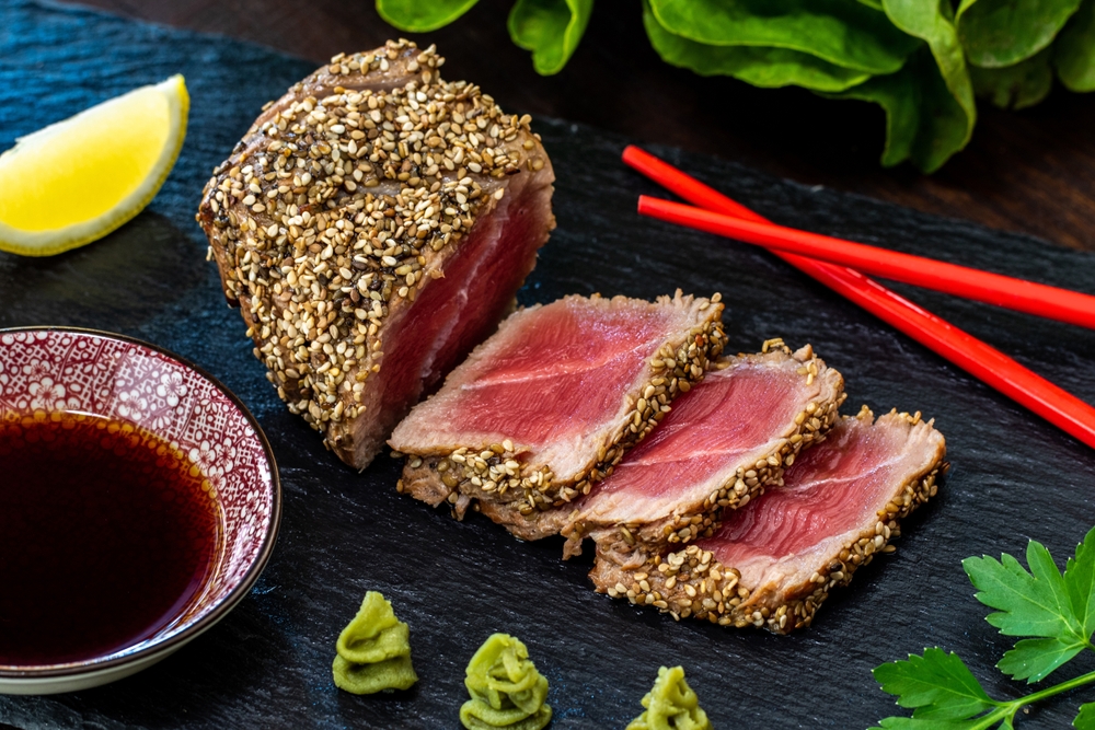 Close up of appetizing sesame crusted tuna steak. Medium rare Yellow fin tuna slices on black slate with wasabi, soy sauce and chopsticks.