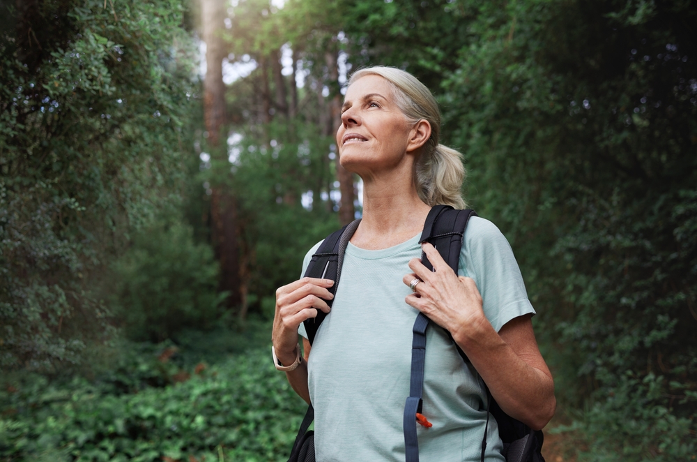 Travel, forest and mature woman on hiking journey, jungle adventure and nature backpack with outdoor explore. Senior camper or hiker person trekking in rainforest or tropical woods for cardio health