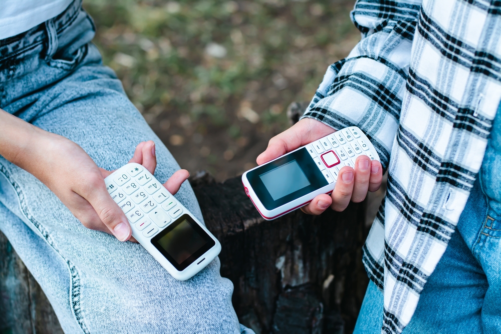 People in jeans hold push-button phones in their hands on their knees