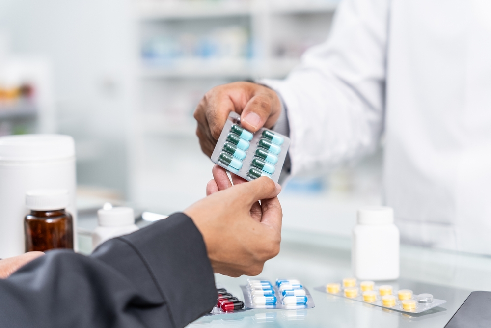 Close up hands of Handsome asian male selling pharmacist and female customer buying medicine in the pharmacy drugstore, hand over capsule pills of medicine from hand to another hand charge.