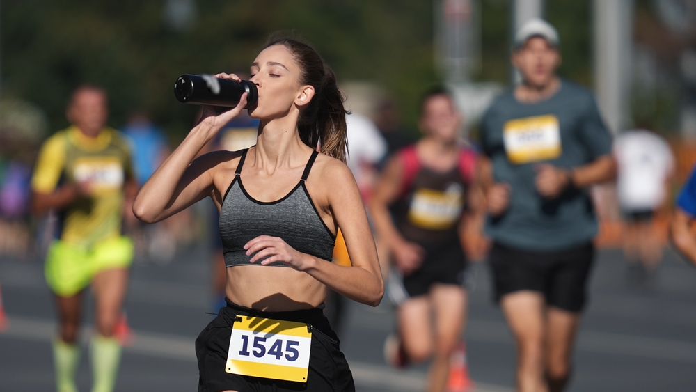 Woman athlete drink water bottle. Thirsty people run long distance. Girl sport runner work out. Adult person train public park. Thirst jogger take break. Jog city arena. Sprinter drinks fresh shake.