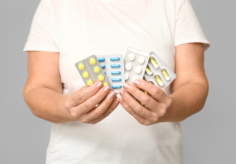 Beautiful mature woman with pills on grey background
