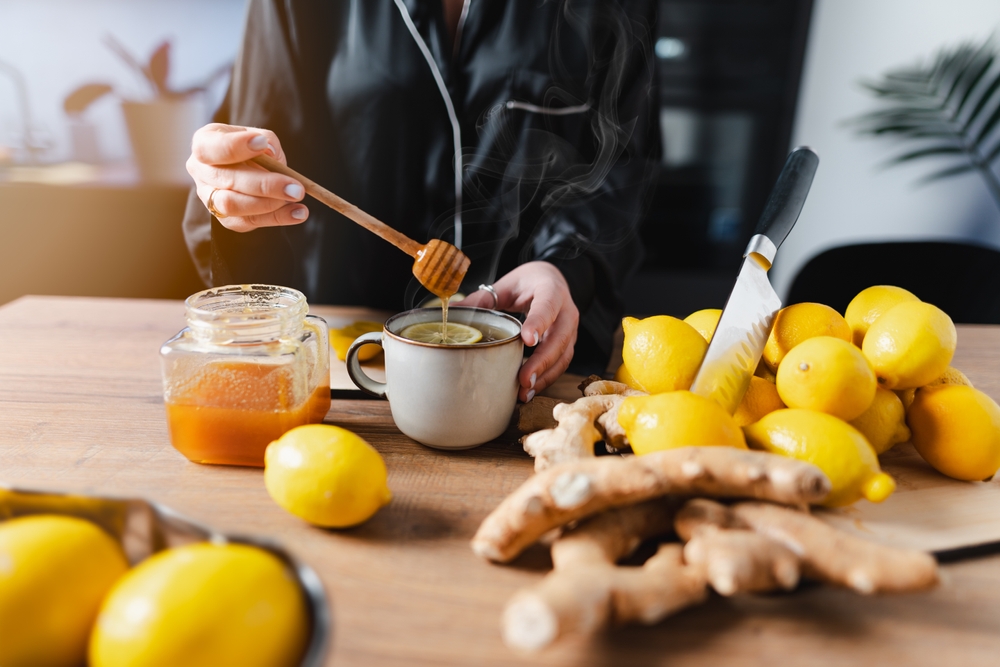 A woman is having a cup of tea on a beautiful morning. Adding honey to the tea with a honey dipper.