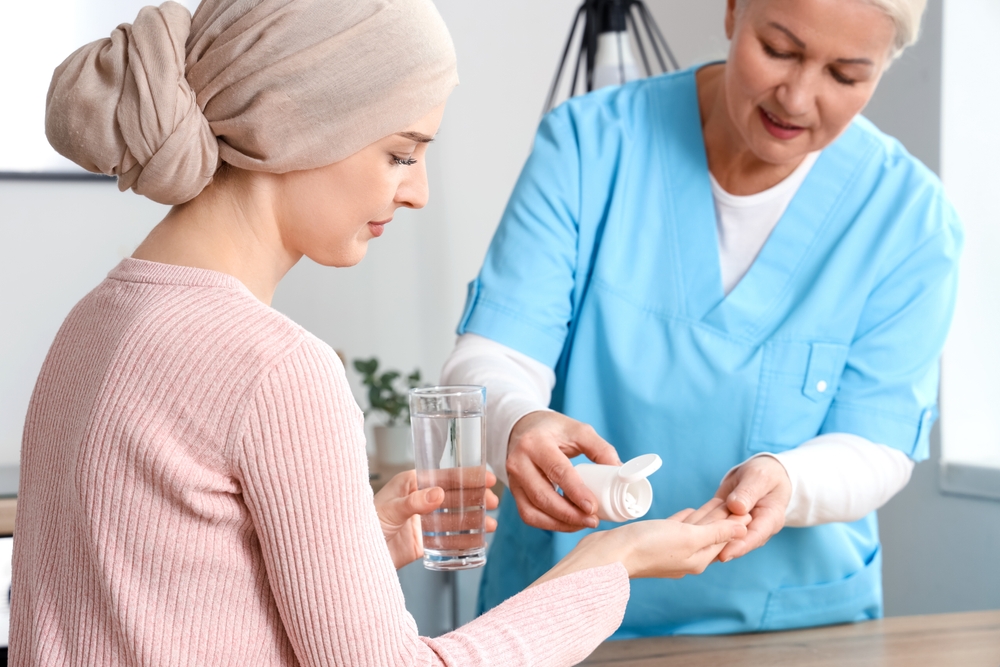 Young woman after chemotherapy taking pills from nurse in kitchen. Stomach cancer concept
