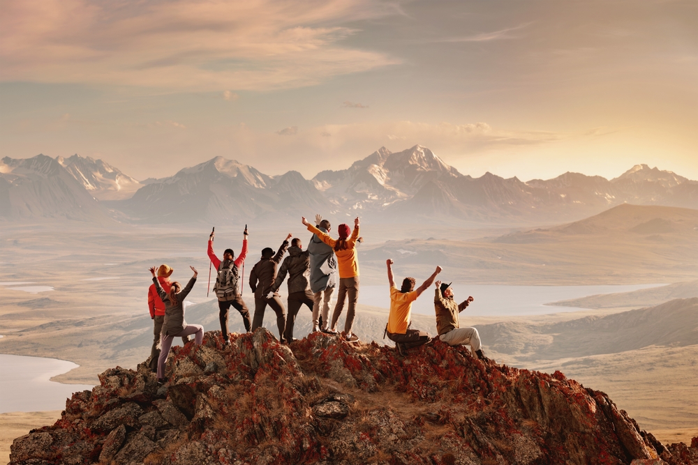 Big group of happy tourists are having fun and greeting sunset at mountain top. Active vacations concept