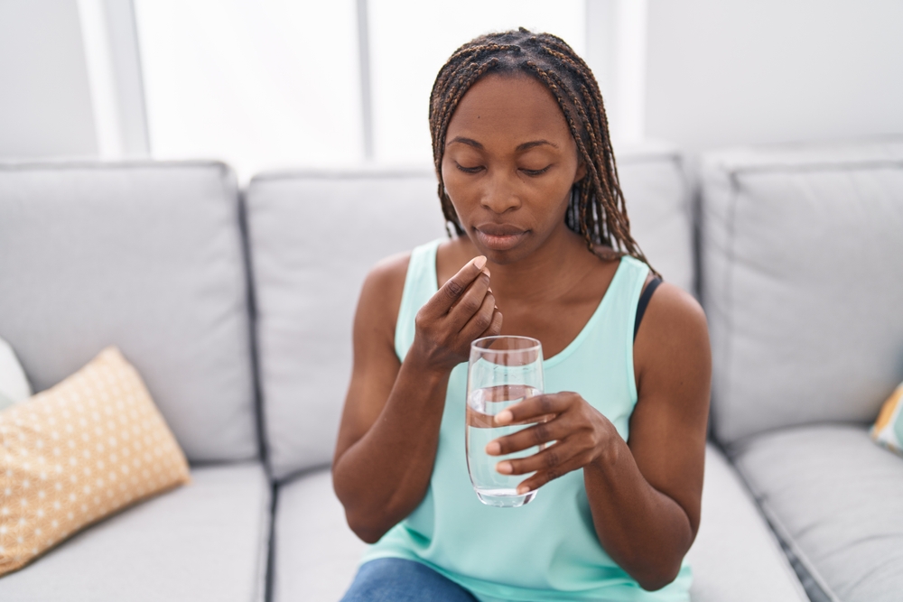 African american woman taking pill sitting on sofa at home
