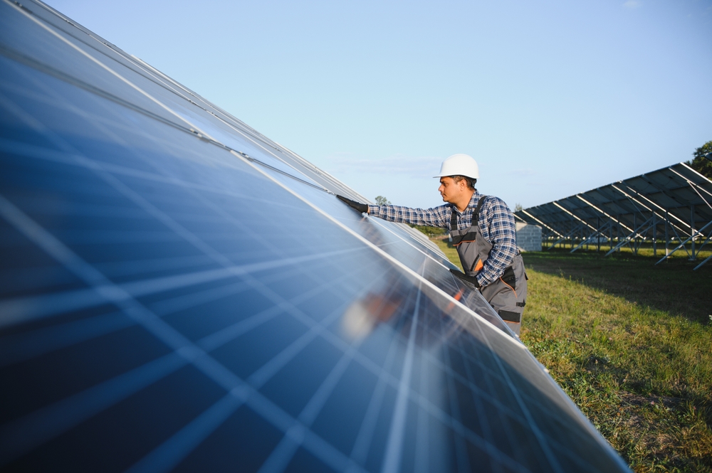 An Indian worker in uniform and with tools works on a solar panel farm.