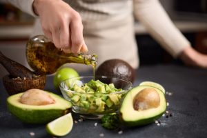 Woman,Pouring,Olive,Oil,Onto,Chopped,Avocado,In,Glass,Bowl