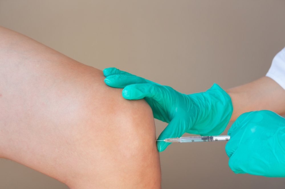 A man at a doctor's appointment with knee pain. Doctor in green gloves gives man an intra-articular injection of hyaluronic acid in the knee joint. Preventing the destruction of the knee joint.
