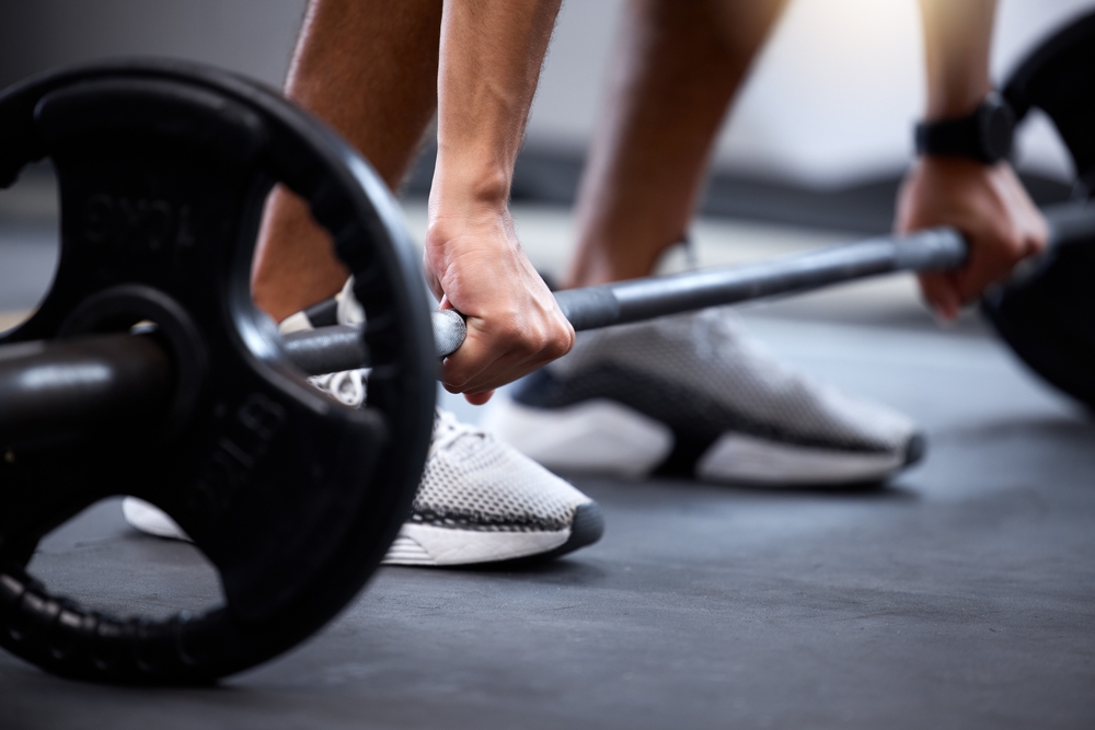 Barbell, fitness and strong hands of man in bodybuilder training for muscle power, legs challenge and workout. Sports, energy exercise and strong body builder in gym with feet zoom on floor or ground
