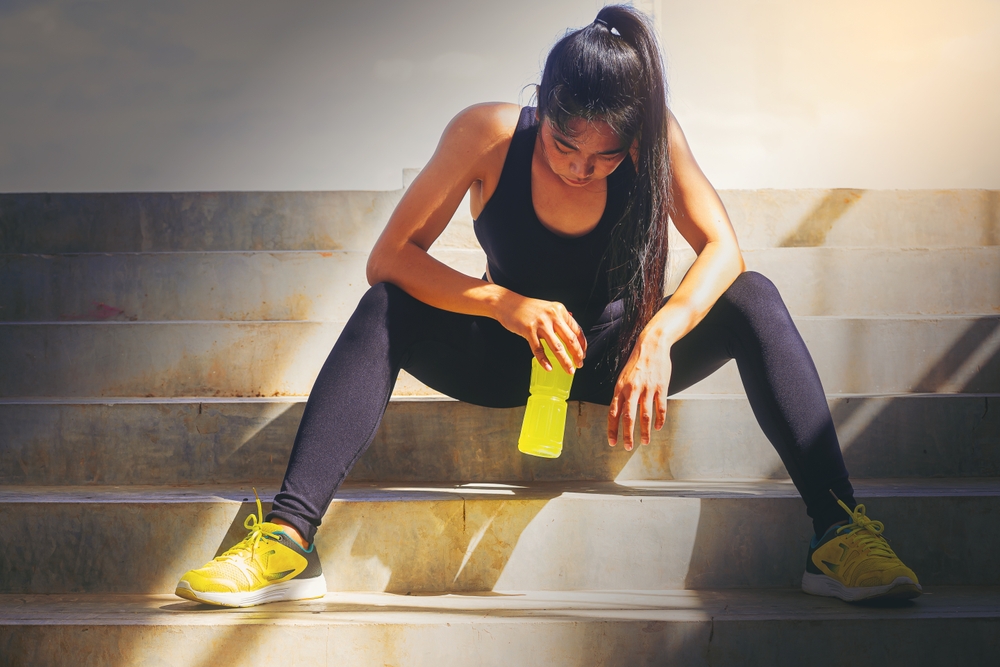 Tired runner woman with a bottle of electrolyte drink freshness after training outdoor workout at the stadium stairway.