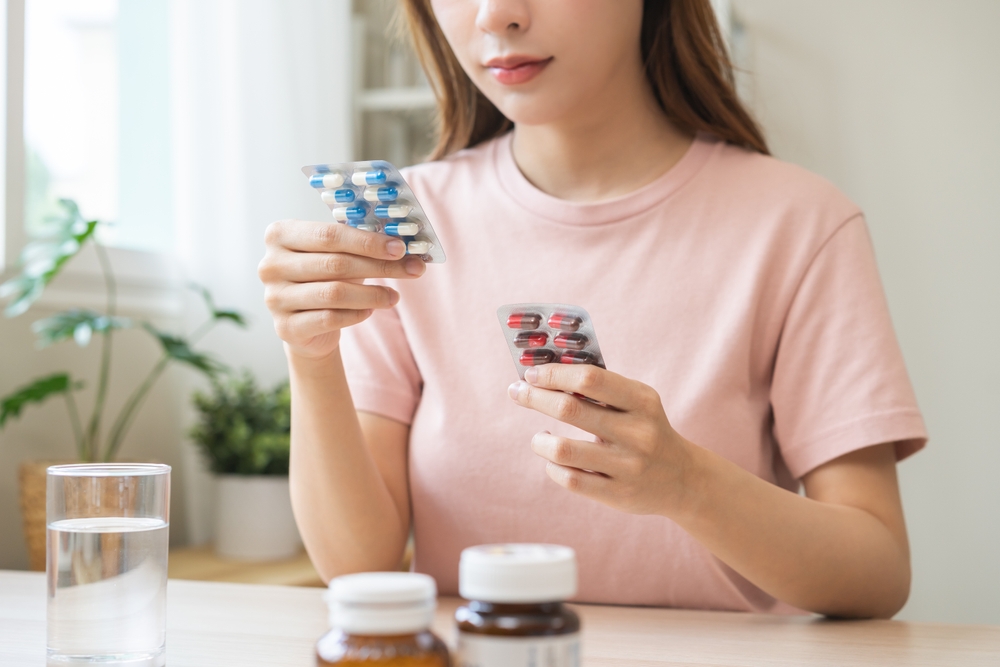Health care treatment asian young woman holding capsules medicine pack reading label text about medical information instructions side effects at medicine on table at home, pharmacy medicament concept.
